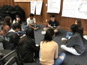 Student Governing Board/Assembly Group seated on carpeted floor having a disussion